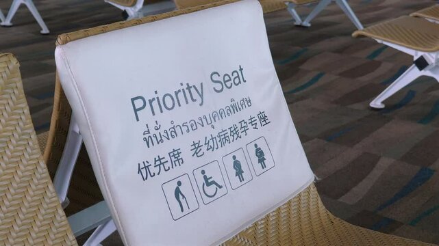 Priority seating area in airport with multilingual signage for passengers with disabilities, elderly, and pregnant women, showing accessibility icons. Accessibility and Inclusivity. Priority Seat sign
