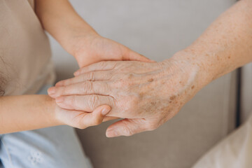 Fototapeta premium Cropped image of grandmother and granddaughter holding hands each other. Age and generation concept. Family relationship, affection, join, unity.