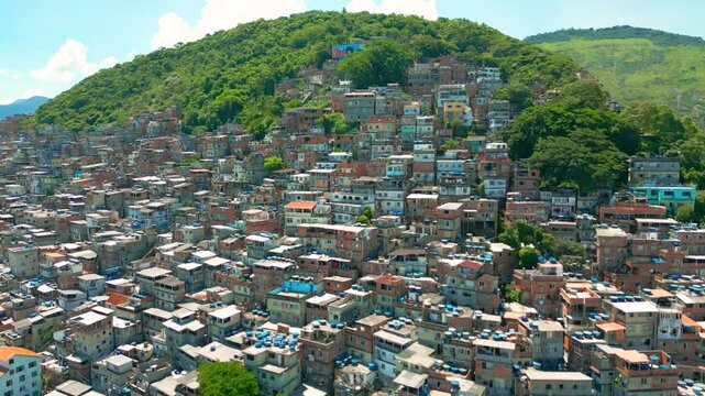 A favela community with colorful buildings, set against lush green hills, under a clear blue sky in Rio de Janeiro, Brazil.