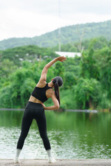 Fototapeta premium A young Asian woman wearing black exercise clothes, has a good figure, is strong, and is warming up. Stretch your legs before your run in a shady park. Exercise concept for health.