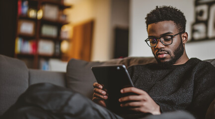 Black man in a cozy living room reading on an ipad