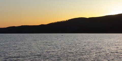A distant view of a small boat on Bracciano Lake at sunset, with silhouetted hills and calm waters in Trevignano Romano, Italy.
