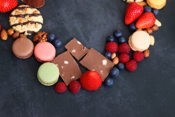 Macarons, chocolate, cookies, berries and various nuts on dark blue background. Selective focus.