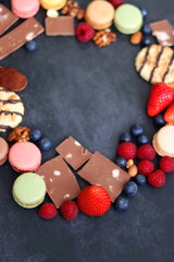 Macarons, chocolate, cookies, berries and various nuts on dark blue background. Selective focus.
