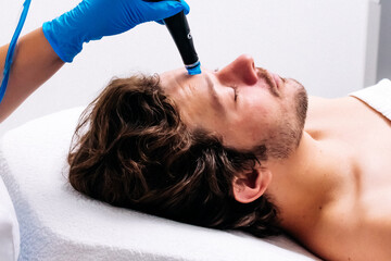 Man receiving a hydrafacial treatment in a modern cosmetic center. Innovative skin hydration and...