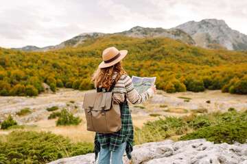 Young woman hiking in autumn landscape with a map, enjoying the scenic views of mountains and...
