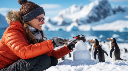 A woman in a red jacket and beanie engages with penguins while building a snowman in a snow-covered landscape accented by snowy mountains, highlighting interaction with wildlife.