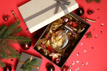 Perfume bottle in gift box and Christmas decor on red background, flat lay