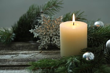 Burning candle, baubles and fir tree branches on wooden table, closeup. Space for text