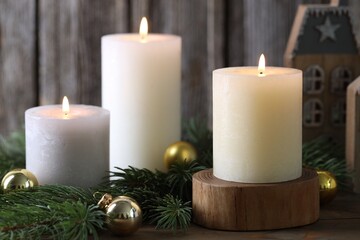 Burning candles, baubles and fir branches on wooden table, closeup. Christmas atmosphere