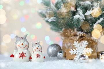 Cute snowman figures in Christmas composition against blurred lights, bokeh effect. Space for text