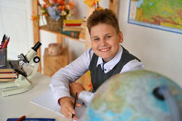 A smiling boy is doing his homework at the table. A student uses a microscope. Elementary school.