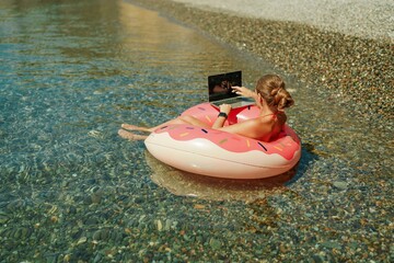Woman laptop sea. Freelancer woman in sunglases floating on an inflatable big pink donut with a laptop in the sea. People summer vacation rest lifestyle concept