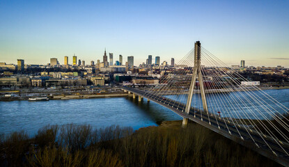 Fototapeta premium Aerial view of Warsaw’s skyline at dawn, with the Świętokrzyski Bridge crossing the Vistula River. 