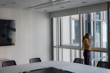 Businesswoman on a phone call in an empty office conference room looking out of the window