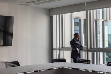 Businessman on a phone call in an empty office conference room looking out of the window