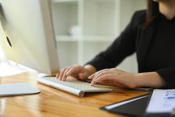 Close up of a businesswoman typing on a computer keyboard, seated at a wooden office desk