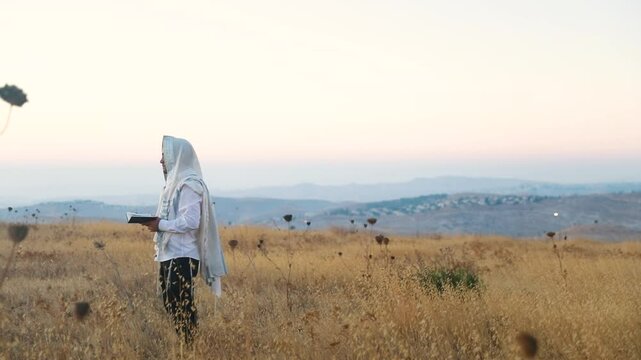A jew prays in a field at sunrise, with tallit and Sidur. Tfilat Shacharit.