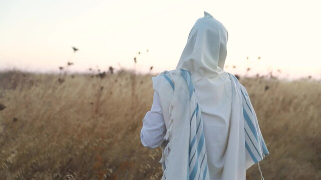 A jew prays in a field at sunrise, with tallit and Sidur. Tfilat Shacharit.
