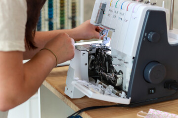 Close-up of a fashion designer adjusting and preparing an industrial sewing machine in a studio with colorful spools of thread in the background. Tailor concept