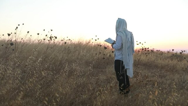 A jew prays in a field at sunrise, with tallit and Sidur. Tfilat Shacharit.