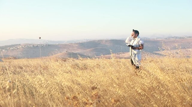 A jew prays in a field at sunrise, with tallit and Sidur. Tfilat Shacharit.