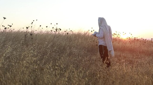 A jew prays in a field at sunrise, with tallit and Sidur. Tfilat Shacharit.