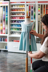 Woman fashion designer adjusting measurements on a dress mannequin in a colorful studio for custom clothing design, vertical image. Tailor and retail concept
