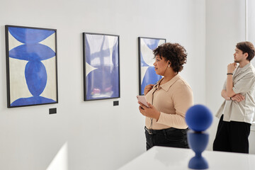 Minimal side view of people visiting modern art gallery or museum and looking at abstract paintings in blue copy space