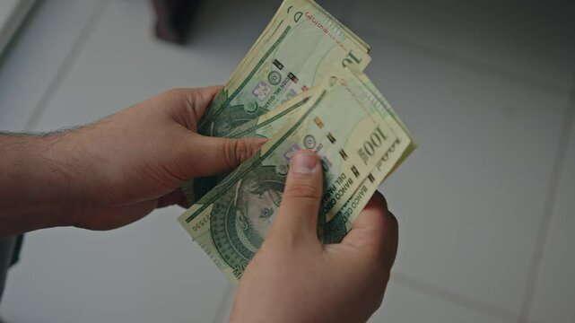 close up of male hands counting a stack of one hundred thousand guaran&iacute;es PYG banknotes a businessman is counting cash the concept of investment, money exchange, bribes, or corruption. selective focus