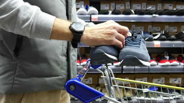 Close-up of a man with a shopping trolley choosing blue sniekers in a shoe store