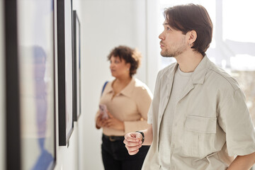 Minimal side view portrait of man looking at paintings while visiting modern art gallery exhibition...