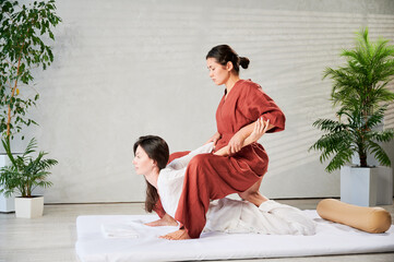 Masseuse making thai yoga massage. Woman therapist doing traditional massage treatment, stretching...