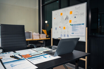 An empty office desk at night with a laptop displaying a business chart, balance sheet, loan calculator, graphs, and monthly budget stats. Blue and black tones, leather office chair.