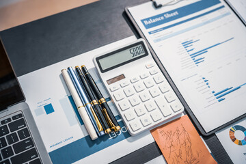 An empty office desk at night with a laptop displaying a business chart, balance sheet, loan calculator, graphs, and monthly budget stats. Blue and black tones, leather office chair.