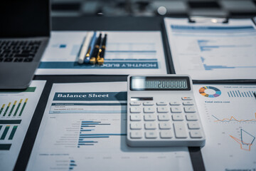An empty office desk at night with a laptop displaying a business chart, balance sheet, loan calculator, graphs, and monthly budget stats. Blue and black tones, leather office chair.