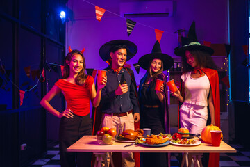 Asian friends, middle-aged man and young woman, enjoy Halloween office party with vampire costumes, fried chicken, grilled food, grape wine, champagne, RGB lights, festive decorations in the night.