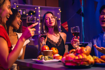 Asian friends, including a middle-aged man and a young woman, enjoy an office party with RGB lights, fried chicken, grilled food, hamburgers, grape wine, and champagne, celebrating together at night.