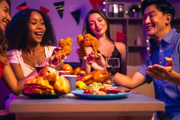 Asian friends, including a middle-aged man and a young woman, enjoy an office party with RGB lights, fried chicken, grilled food, hamburgers, grape wine, and champagne, celebrating together at night.