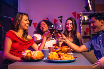 Asian friends, including a middle-aged man and a young woman, enjoy an office party with RGB lights, fried chicken, grilled food, hamburgers, grape wine, and champagne, celebrating together at night.