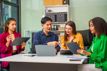 Asian colleagues, middle-aged man and young woman, happily collaborate in office workplace. They gather around laptop, discussing project management, startup plans, teamwork paper stacks on desk.