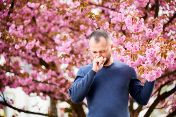 Man allergic suffering from seasonal allergy at spring in blossoming garden at springtime. Bearded...