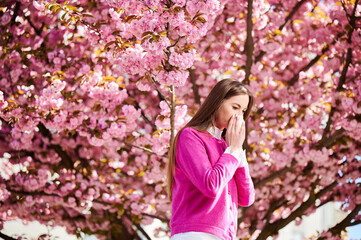Woman allergic suffering from seasonal allergy at spring in blossoming garden at springtime. Woman...