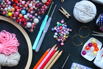 Colorful beads, coloring pencils, glitter, needles, string, hoop, tape and scissors on dark...