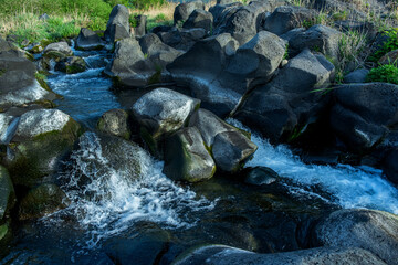 Naturally occurred rocks and streams. A rock that has special and unique frame. There are small plants growing in the crevices of the rocks.