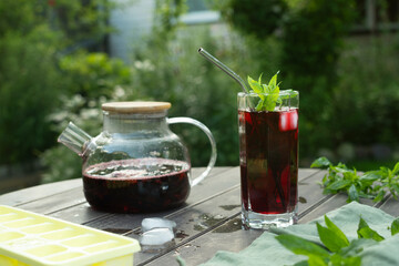 Glass of summer cold berry tea on wooden table outdoors. 