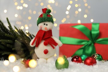 Funny snowman figure and other Christmas decor on artificial snow against blurred lights
