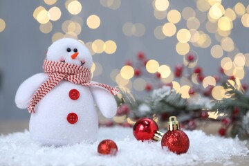Funny snowman figure and Christmas balls on artificial snow against blurred lights