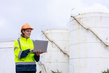 Engineer wearing green uniform and helmet standing workplace hand holding labtop oil refinery background..
