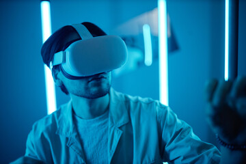 Portrait of young man wearing VR headset in modern art show interacting with blue neon lights enjoying digital mixed reality experience